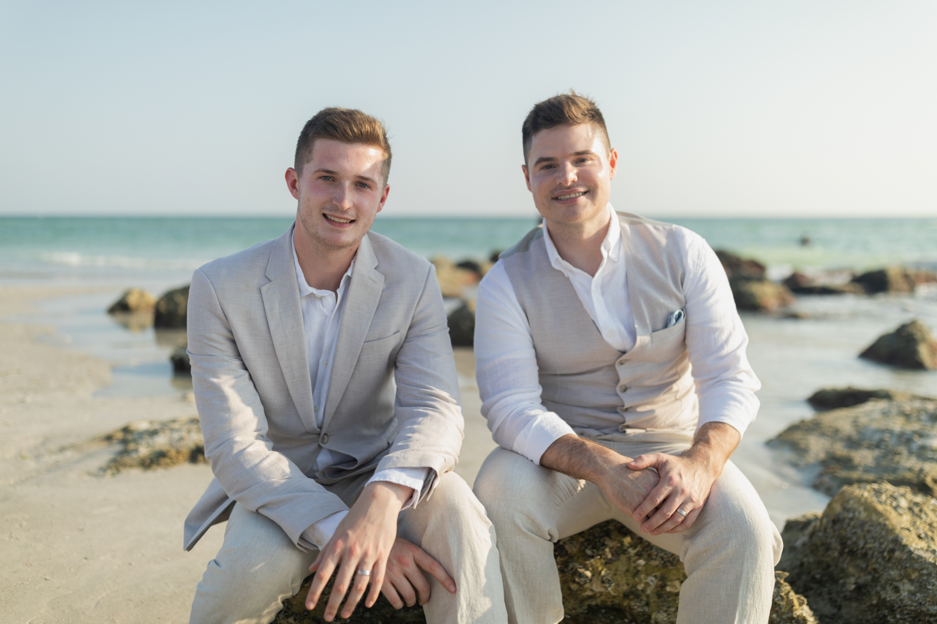 Joel and Owen on their 2023 wedding day, seated on rocks at Redington Beach, Florida.