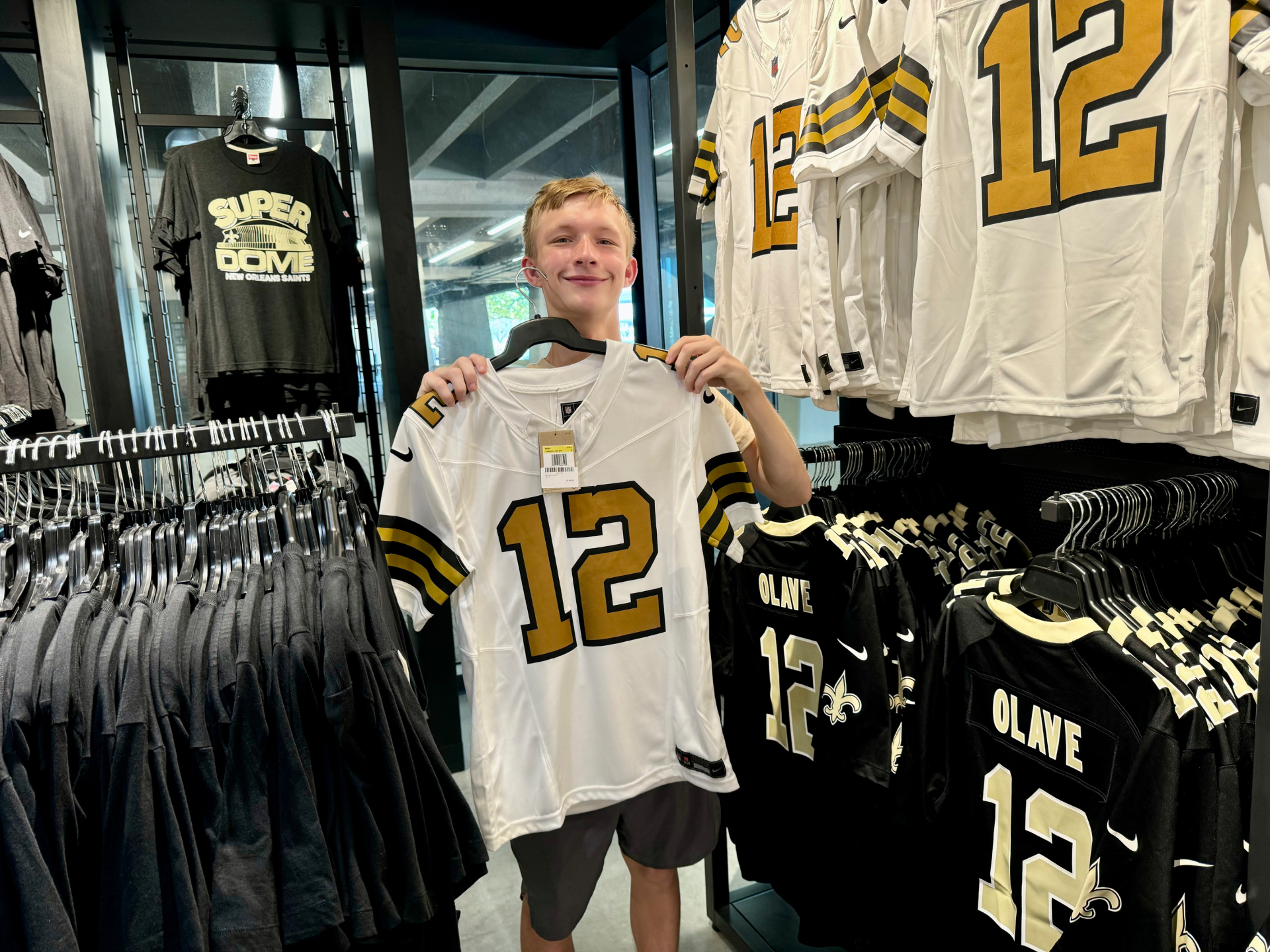 Joel and Owen's teenage son holding up a football jersey in a team store.